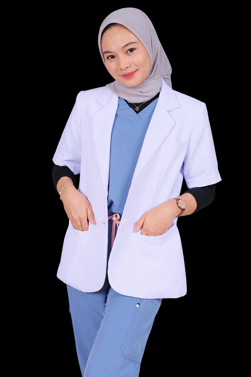 dr. Shinta Anni Fadilla tersenyum mengenakan hijab abu-abu, jas dokter, dan seragam medis biru
